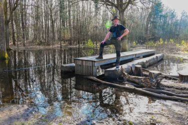 Jan poseert met de verrekijker op de banken en de eettafel die in het water staan opgesteld in speelbos Het Joekelbos.