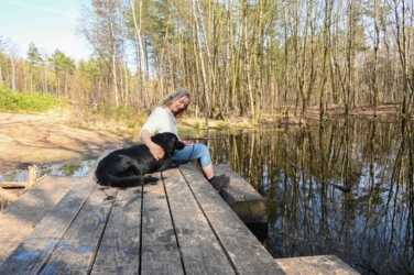 Helena en mazzel zitten op de gigantische picknicktafel in het Joekelbos. Deze tafel staat in het water en er kan dus niet op de zware eikenhouten banken gezeten worden. In het water weerspiegelen de bomen van het omliggende bos.
